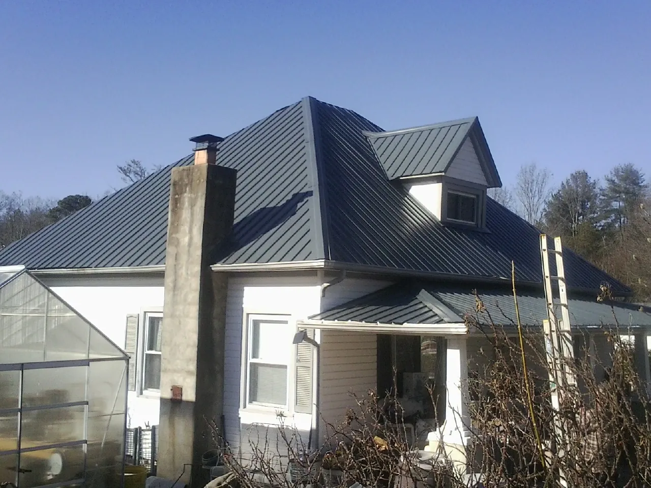 Dark blue standing seam metal roof on a white farmhouse with dormer — Slate & Tile Roof Repair by Roofing Brothers in Himrod