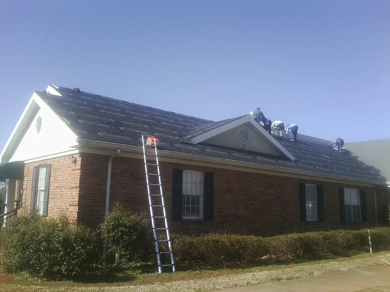 Crew tearing shingles off a brick ranch roof with a ladder set — Emergency Roof Repair work by our crew in Himrod