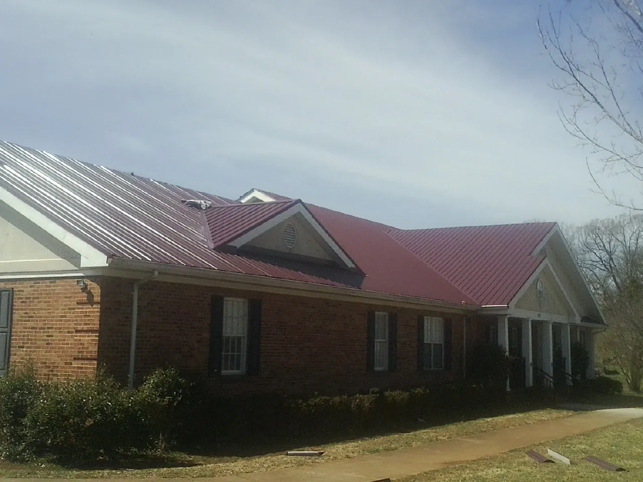 Red metal roof with gabled entries on a long brick building, from a Hail Damage Roof Repair job in Himrod