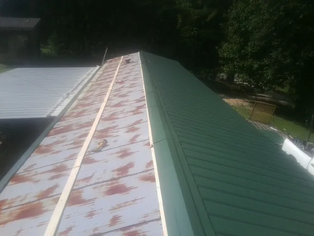 Old rusted panels beside newly installed green metal roofing — Wind Damage Roof Repair by Roofing Brothers in Himrod