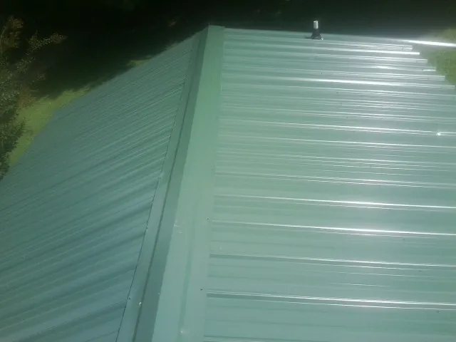 New green metal panels meeting at the ridge of a roof — Flat Roof Repair work by our crew in Himrod