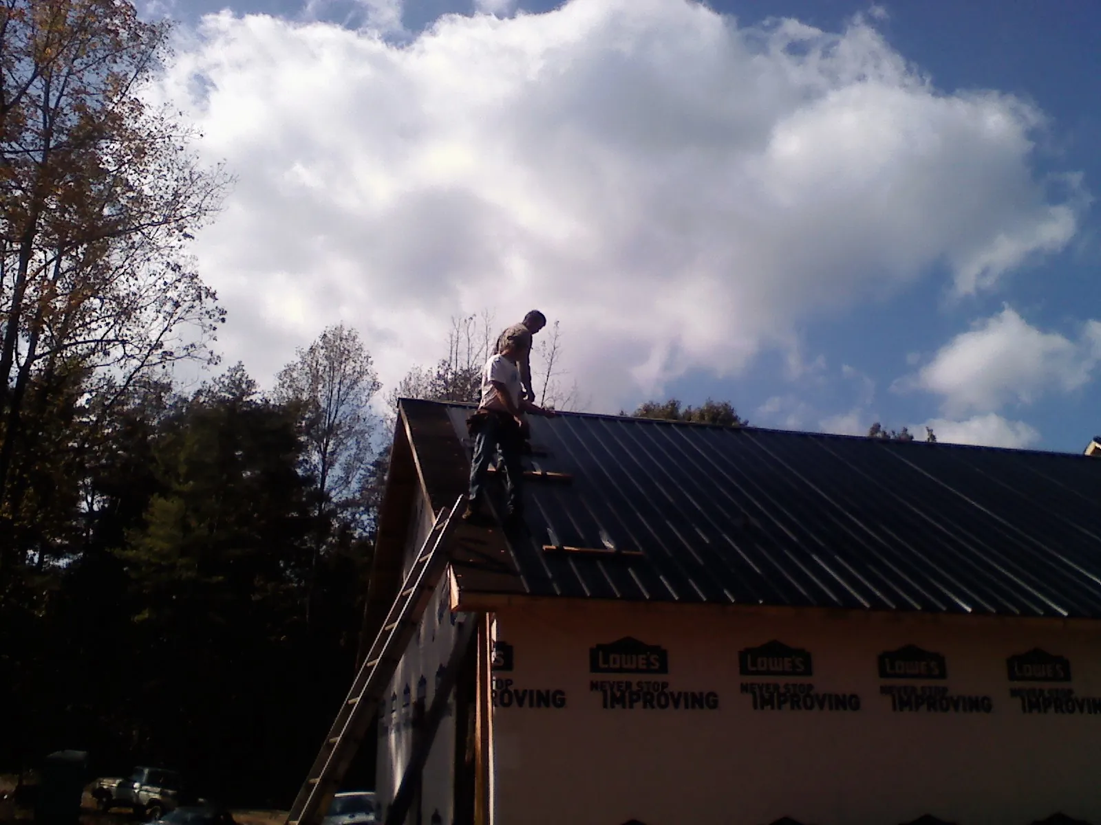 Roofer fastening dark metal panels high against a cloudy sky, from a Roof Inspection job in Himrod