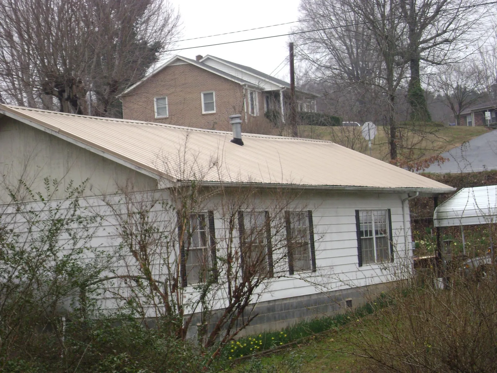 Tan metal roof on a white sided house set into a hillside — Commercial Roofing by Roofing Brothers in Himrod